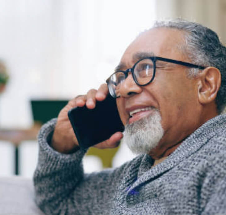 An elderly gentleman holds a cellphone to his ear while smiling and engaging in conversation.